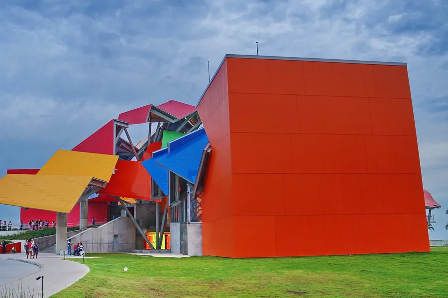 Biomuseo's colorful angular roofs and red wall designed by Frank Gehry, on green lawn