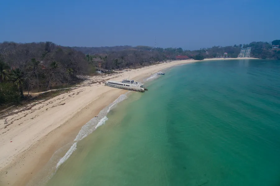 Turquoise water and a long pale sand beach on Contadora island, with a boat beached on the shore