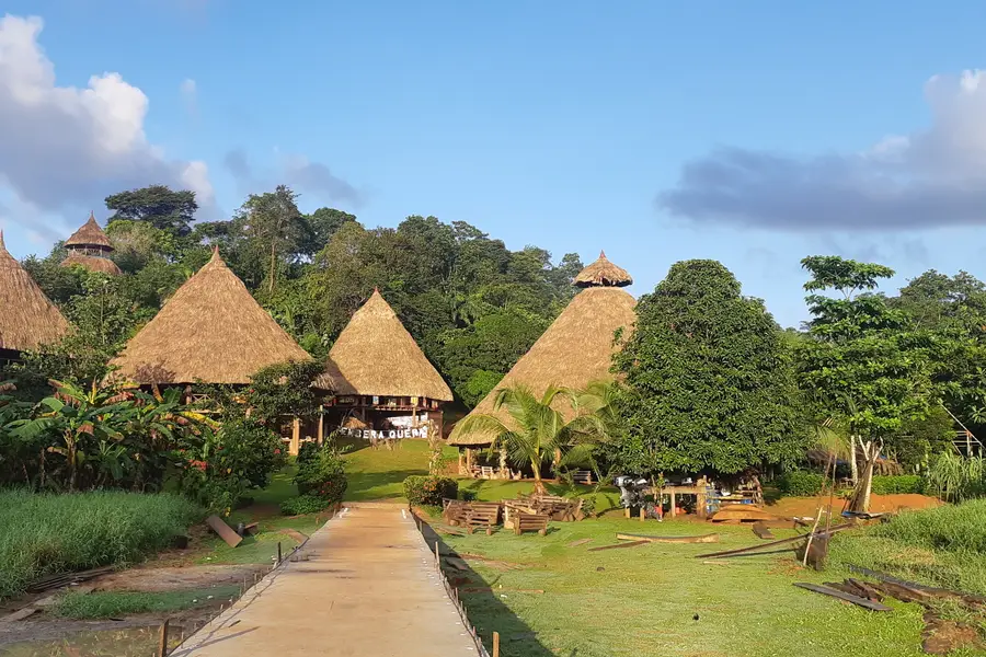 Thatched-roof huts at an Embera village along a dirt path under blue sky