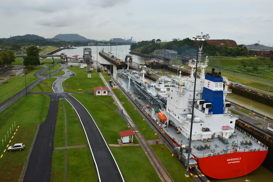 Tanker with a red hull entering the Miraflores Locks beside green lawns and hills