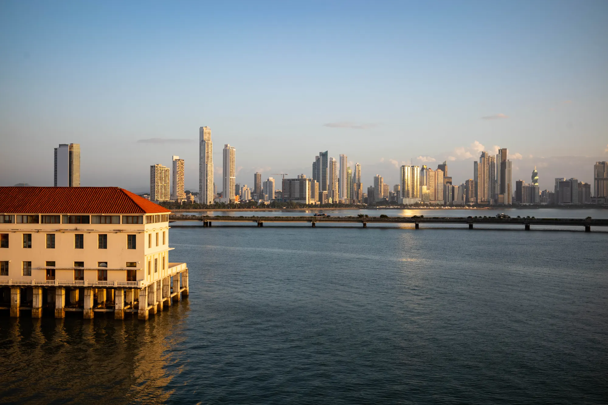 Panama City skyline across the bay at golden hour, stilted colonial building at left