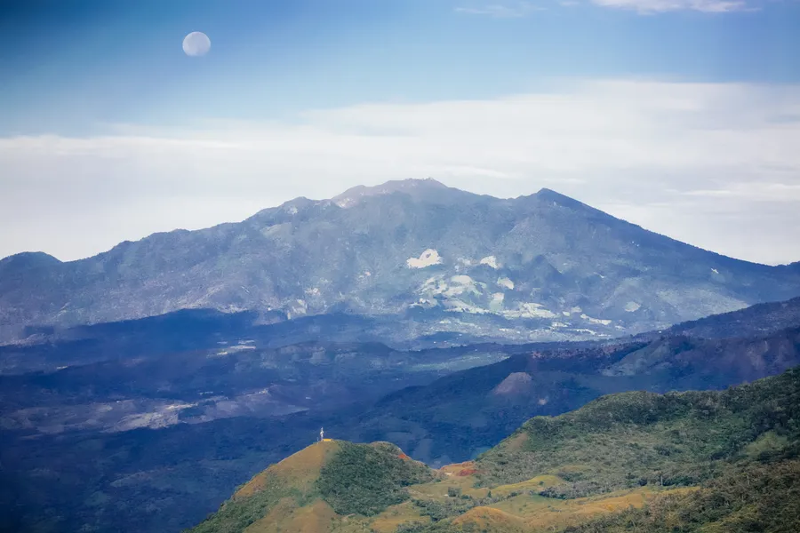 Volcan Baru's hazy blue summit above green foothills with a pale moon above